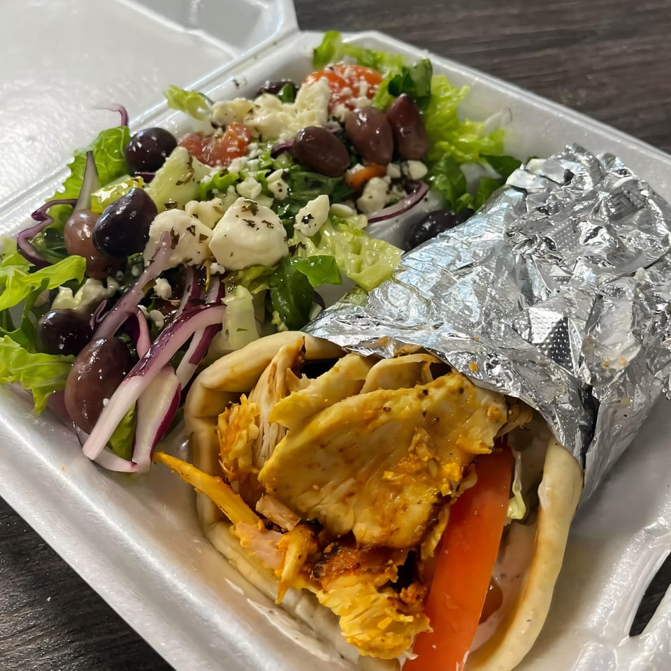 Habibi Mediterranean Grill's chicken gyro with a side Greek salad in a white takeout container.