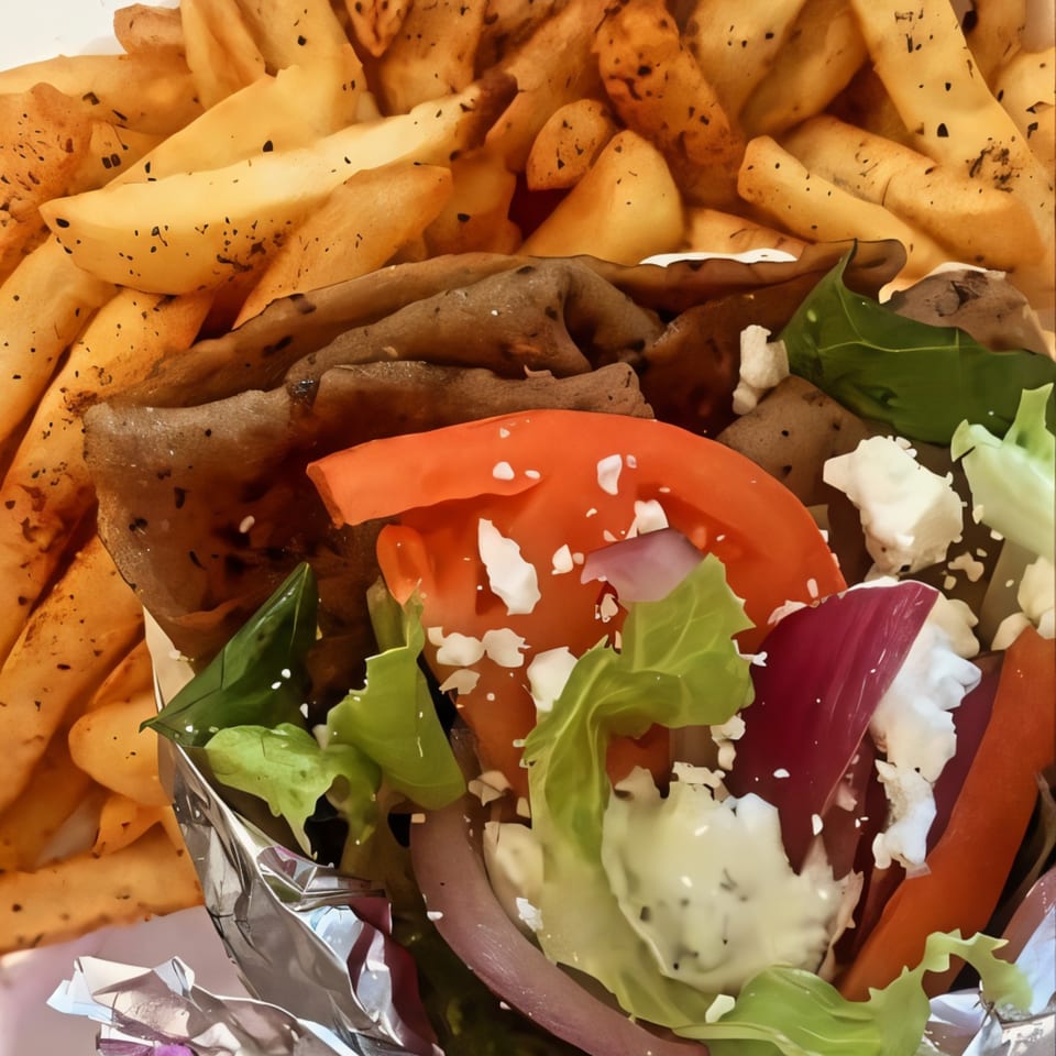 A Mediterranean gyro with meat, lettuce, tomato, feta, and sauce, served with seasoned fries.