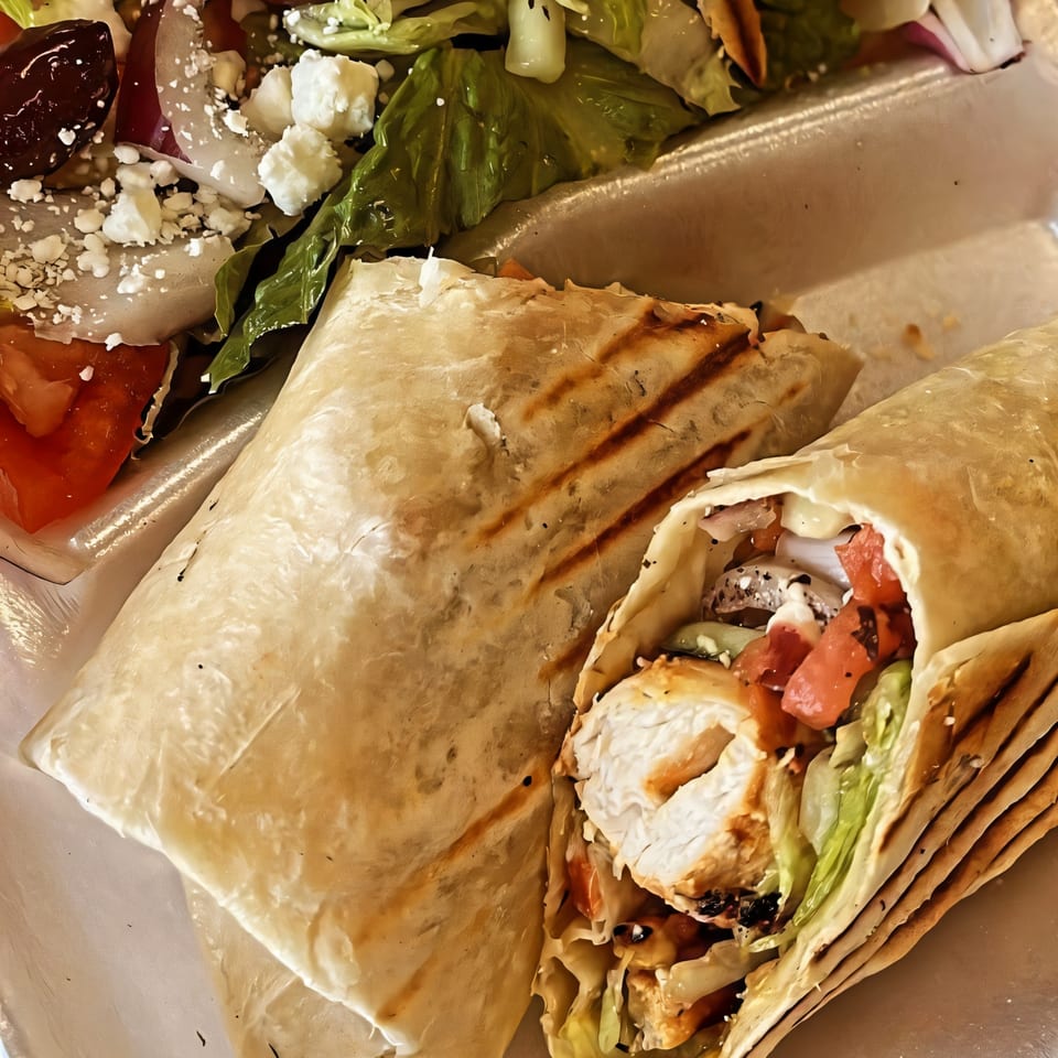 Two grilled chicken wraps with lettuce, tomatoes, and sauce, served with a side salad.