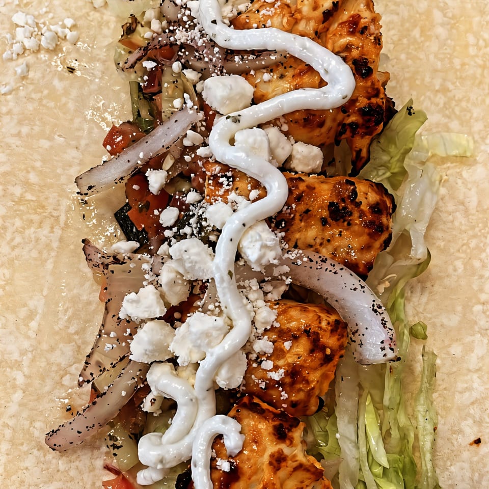 Close-up of a Habibi Mediterranean Grill wrap with chicken, lettuce, onions, feta, and white sauce.